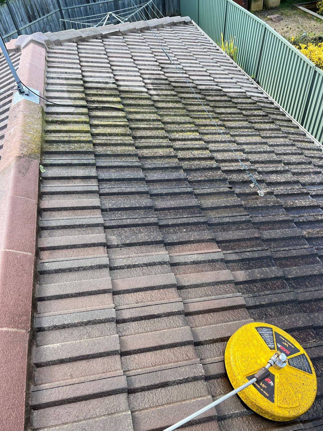 A grey tile roof being pressure cleaned, with a clear line between the dirty and clean sections