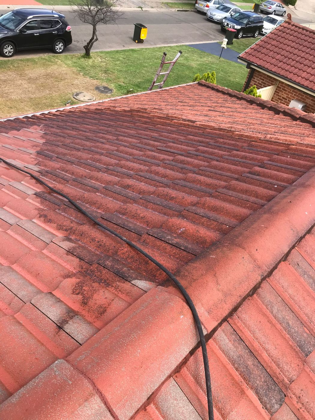 A faded red tile roof part way through cleaning, half dirty and half like new