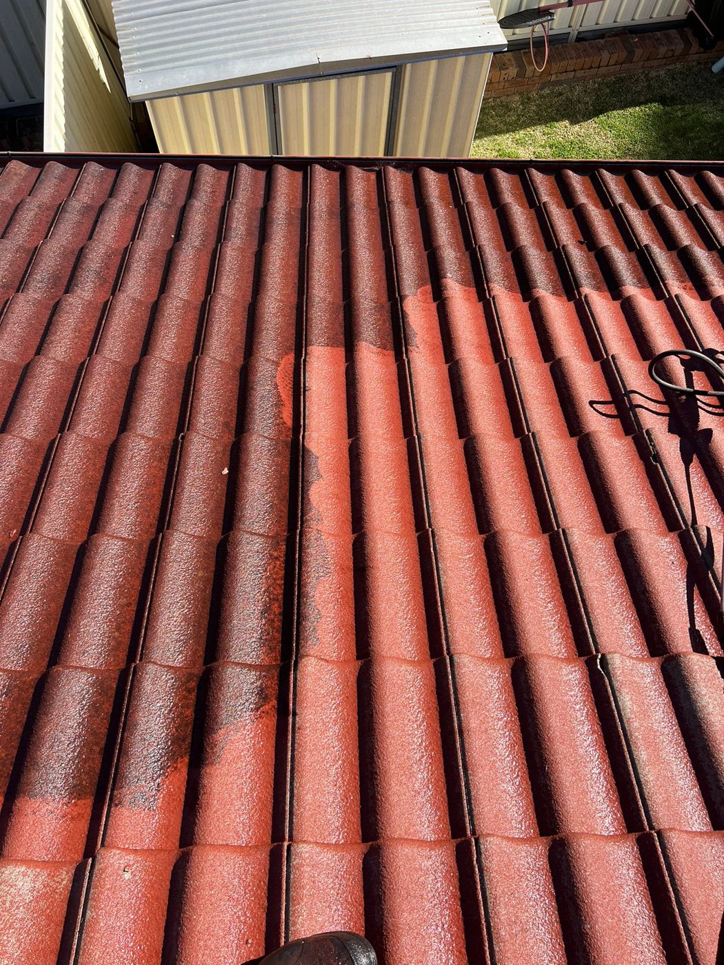 A red tile roof with a freshly cleaned patch showing the colour returning